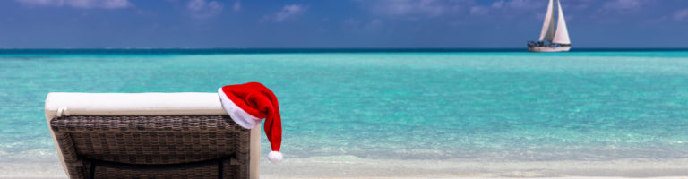 A sun lounger on a tropical beach with a red Santa Clause hat