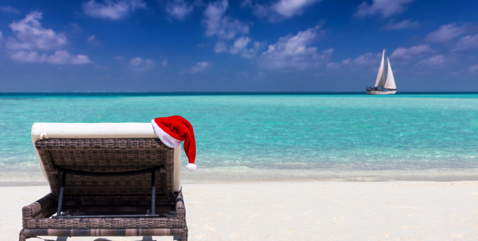 A sun lounger on a tropical beach with a red Santa Clause hat