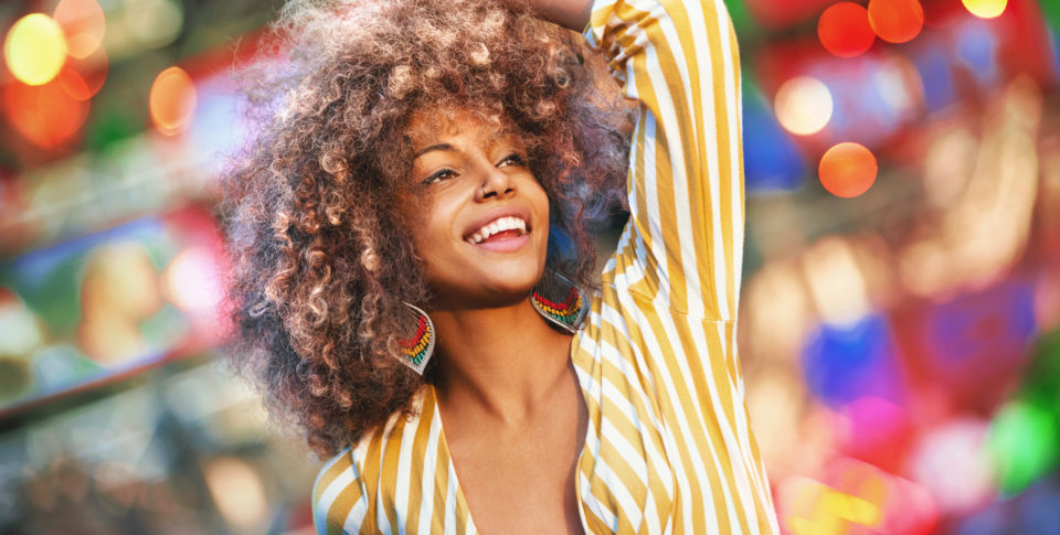 Closeup of an attractive mid 20's black woman dancing at an open air concert on a summer afternoon. She's completely enjoying her favorite kind of music. Blurry stage lights in background.