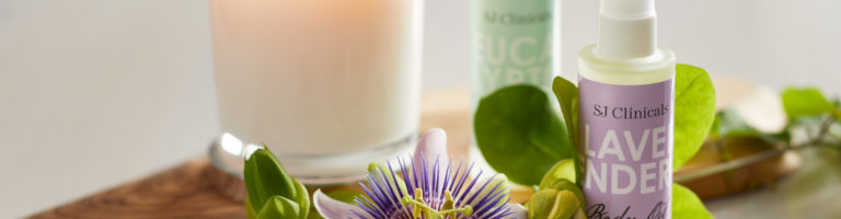 A lit white candle on a wooden tray decorated with eucalyptus and lavender spray and a purple flower